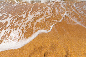 Fototapeta na wymiar Sea wave with white foam on yellow golden sand. Summer ocean holiday background