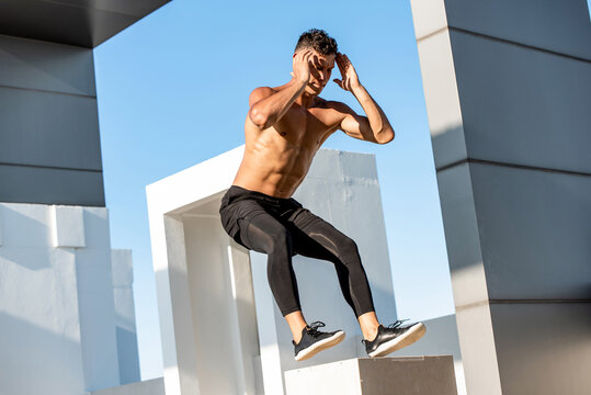 Fit shirtless sports man jumping up to plyometric wood box outdoors on building rooftop, home bodyweight workout exercise concept
