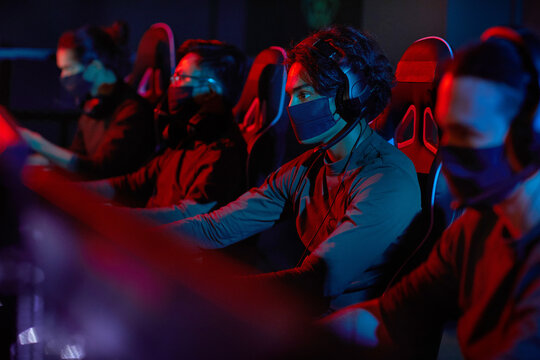 Group of developers in protective masks sitting in front of computers and working in dark office