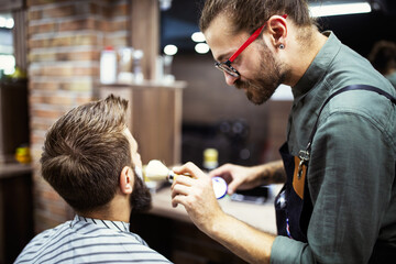 Happy young handsome man visiting hairstylist in barber shop salon