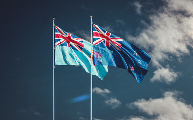 Waving flags of New Zealand and the Fiji Island at blue sky. A symbol of political and economic relations between two countries. Partnership and competition in the world stage.