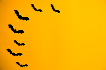 Silhouettes of black bats made of paper on orange background. Halloween greeting template with copy space. Flat lay for your design.