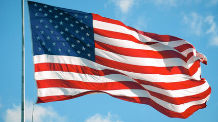American Flag blowing in the wind with a blue sky background. USA American Flag. Waving United states of America famous flag in front of blue sky. Memorial Day, Independence Day - American concept.