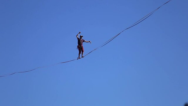 A man walks along the highline against the blue sky, Highliner goes on a stretched sling, Tightrope walker, A man catches balance.