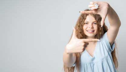 Photo of funny woman smiling and making photo frame with fingers. Human emotions, facial expression concept. Copy space