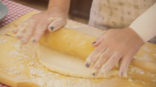 A woman's hands thinning the dough for a focaccia (a flat oven-baked Italian bread product) with a wooden rolling pin. Angled shot.
