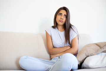 Woman in painful expression holding hands against belly suffering menstrual period pain,sitting sad on home bed, having tummy cramp in female health concept