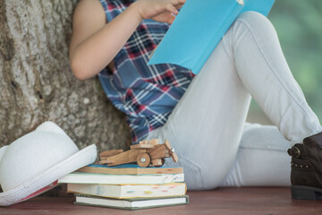  little asian girl reading a book under big tree. children and science. blurred background. learning the imagination and dreams of rural child. studying at home.