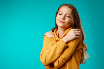 Young peaceful woman hugging herself with eyes closed