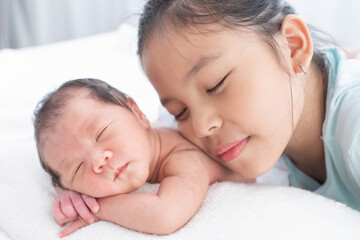 little sister hugging her newborn brother. toddler kid meeting new sibling. love, trust and tenderness. cute girl and new born baby boy relax in a white bedroom. family with children at home.