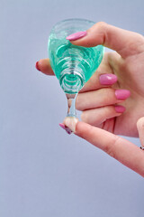 Woman's pouring lotion gel on her finger. Close-up female hands squeezing green transparent shampoo from a small bottle.