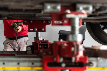Expert senior mechanic repairing a car after a street crash. Details and focus on hands controlling the mechanical lift. Blurred foreground, natural light. Occupation and job concept. Global economy 