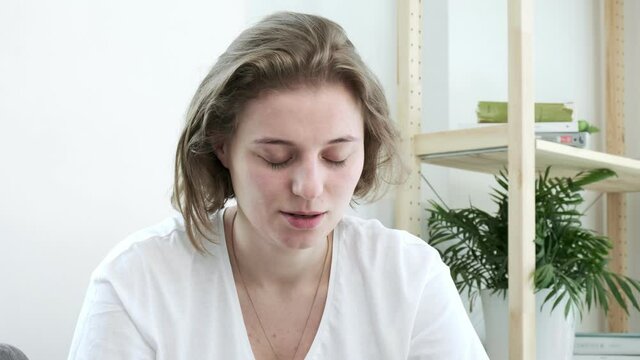 upset young caucasian short-haired woman in white t-shirt closes her eyes, sighs, exhales. closeup portrait of emotional lady with wet eyes at home