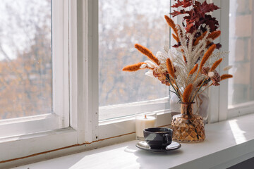 Cup of tea, flowers in vase on the window sill in morning light. Home decoration concept, fall colors, copy space.
