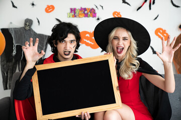 Young caucasian peoples in scary costumes or vampire clothes holding a blackboard, Halloween concept