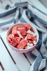 Delicious summer salad with watermelon and feta cheese on white bowl with striped towel on wooden white plate