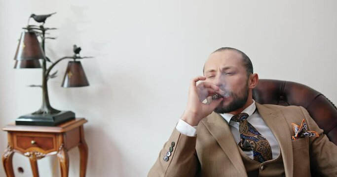 Solid rich in an expensive suit man smokes at his office at a wooden table