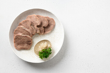 Sliced beef tongue delicacy with natural horseradish sauce isolated on a white table. View from above. Space for text. Juicy tender meat a great appetizer.