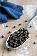 Balls of black pepper in a spoon on rustic background