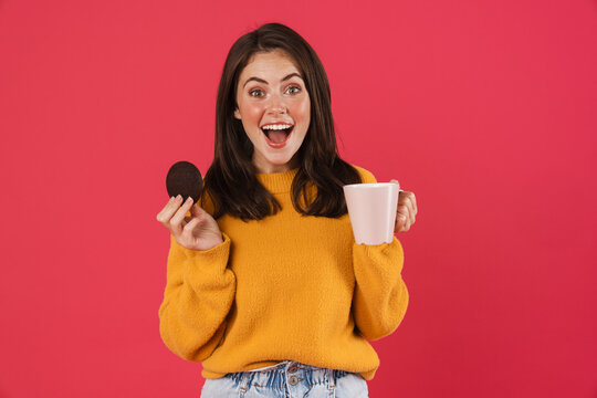 Image of excited caucasian girl drinking coffee with cookie