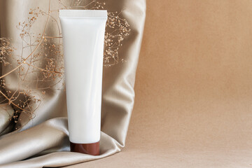 Closeup white tube of moisturizing niche luxury cream on background of beige fabric drapery....