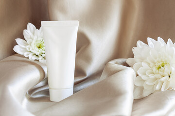 Closeup white tube of moisturizing luxury cream on background of beige gray fabric drapery. Cosmetics, products for care and personal hygiene concept. Minimalistic packing, branding.