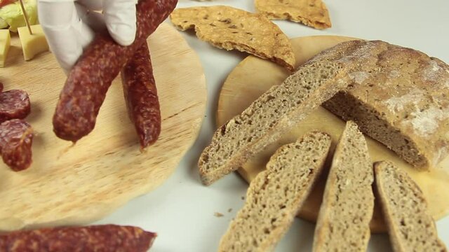 slider view of chefs hands serving a typical South Tyrolean snack plate like Tyrolean smoked sausage on a wooden cutting board accompanied by kaminwurz and paarl type bread