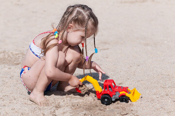 joyful three-year-old girl plays with a machine in the sand on the beach