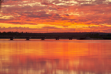 The bright sunset is reflected in the smooth water of the lake.
