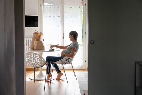 Pregnant woman eating fresh fruits in kitchen