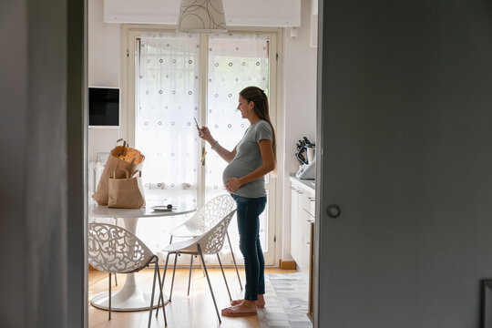 Young pregnant woman using smartphone at home