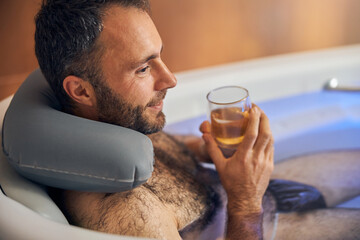 Cheerful young man taking bath and drinking wine