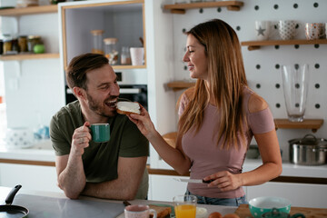 Young couple making breakfast at home. Loving couple eating sandwich in kitchen..