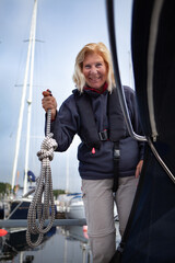 Happy blonde senior woman holding a rope on a sailboat wearing a life jacket