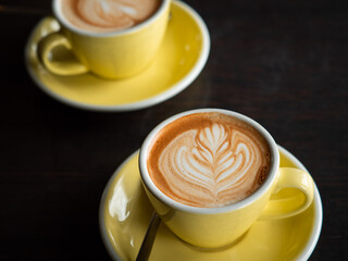 cup of coffee with leaf art in a yellow cup on yellow saucer on a dark table