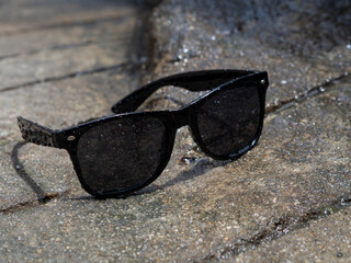 Black Sunglasses On a wet grey road in sunny weather
