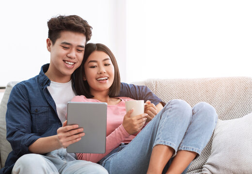 Happy Chinese Couple Using Digital Tablet Relaxing At Home