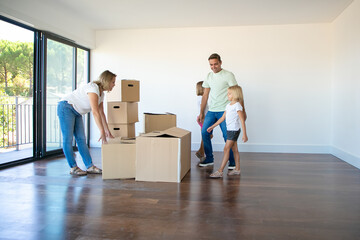 Happy parents and daughters opening boxes and unpacking things in their new empty flat . Real...