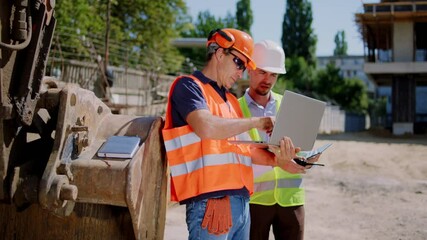 Middle-aged foreman and engineer guy with a protective uniform using the laptop to check the construction of building they have a discussing concentrated. 4k