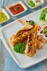 Turkish tantuni in white plate on wooden table, served with various sauces and chips.
