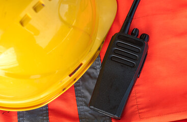 Top view of walkie-talkie, yellow helmet hat laying on orange signal vest.
