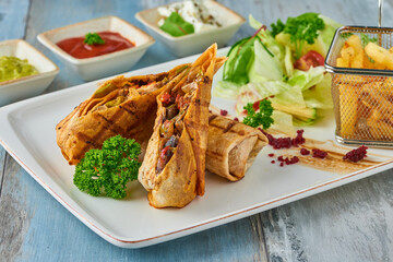 Turkish tantuni in white plate on wooden table, served with various sauces and chips.