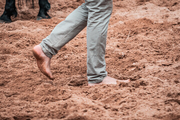 Horse whisperer walking barefoot on the sandpit. Moments before the show begins, natural feeling with the ground and the animal. Rodeo and ranch lifestyle, trainer, equestrian sports moment.