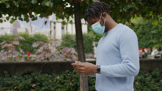 Young black male in a face mask walks and uses his phone in the city, in slow motion
