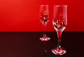 Two champagne glasses with small Christmas balls inside against red background