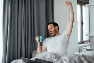 Fototapeta na wymiar Young man watching movie in bed. Handsome man enjoying in morning