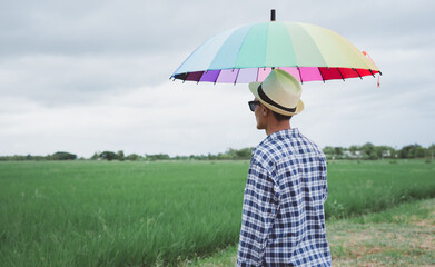 Man holding rainbow umbrella with nature background.