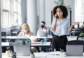 Talking with client in workspace and return after quarantine. Employees work in office with laptops and antiseptics, focus on african american woman