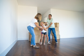 Excited happy girls tickling each other and laughing. Happy family couple and two kids having fun together while moving into new apartment. Full length. Real estate purchase concept