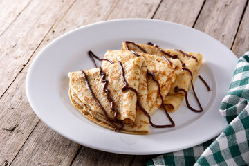 Sweet crepes with chocolate on wooden table. 	